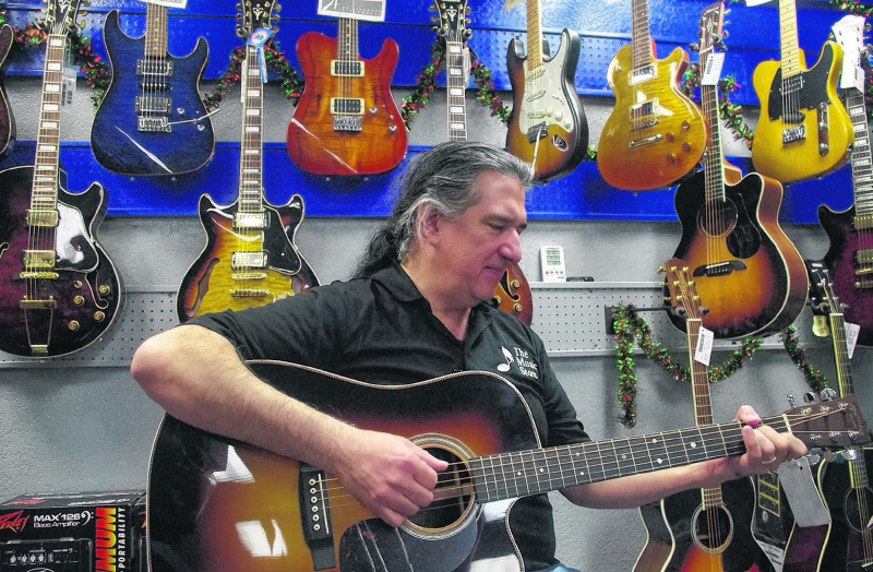 J.P. Escobedo, co-owner of The Music Store, strums one of the guitars on display at the longtime East Valley location. 