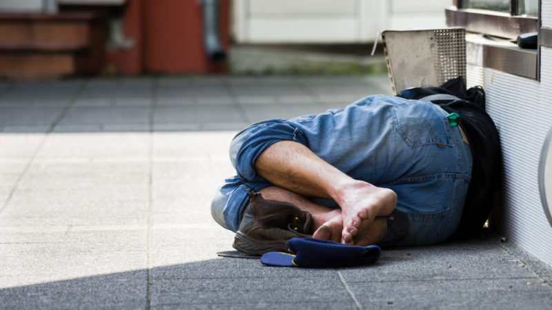 homeless man laying on side of street